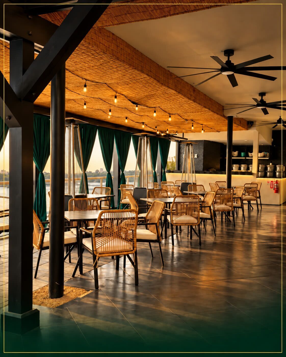 The dining terrace in late sun, rattan chairs and gold lights over dark tables